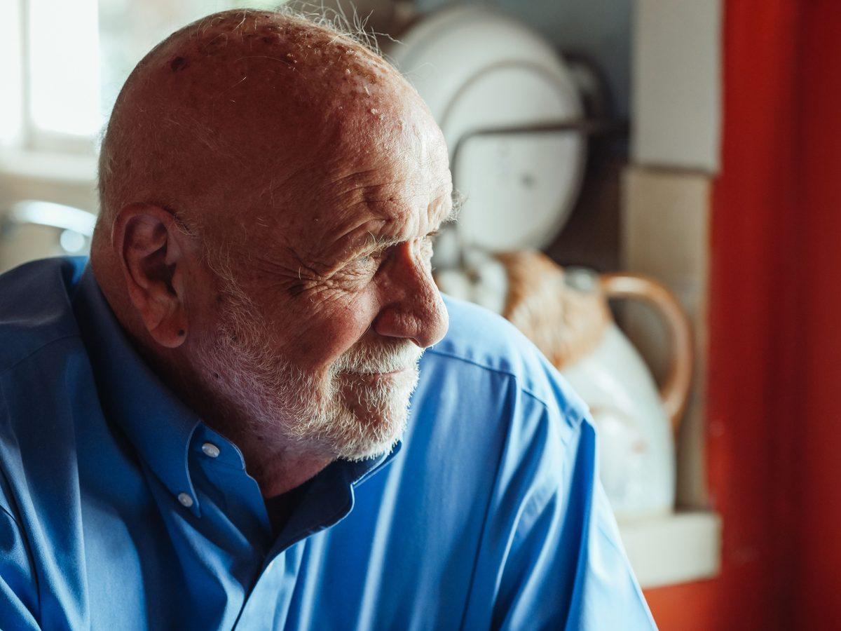 Older man looking thoughtfully out of a window at home